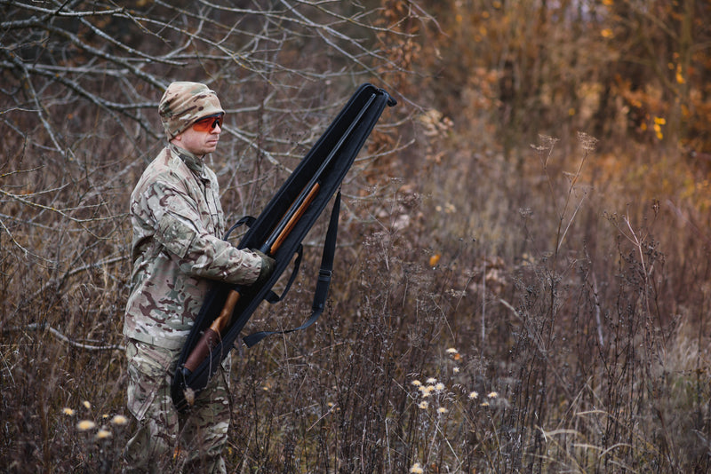 Hunter in camouflage gear holding a rifle in a forest setting testing outdoor gear in the field — banner for Gear Guides & Reviews category, Fieldborne Gear.