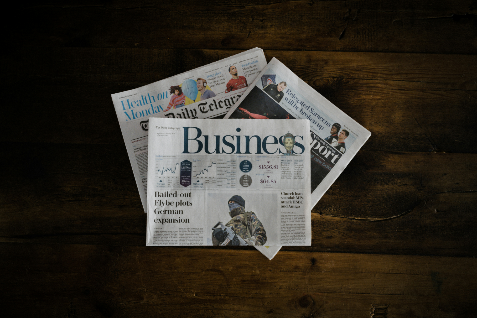 Newspapers on a wooden surface with 'Business' section visible Fieldborne Gear announcement banner — brand news, updates, and product milestones.
